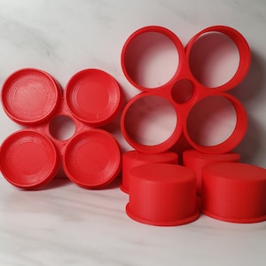 May include: A set of six red plastic circular molds, arranged in two groups. The first group is a flower-shaped mold with four circles, and the second group is a smaller flower-shaped mold with three circles.