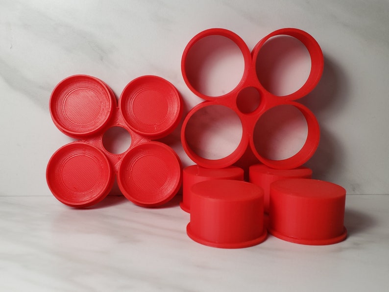 May include: A set of six red plastic circular molds, arranged in two groups. The first group is a flower-shaped mold with four circles, and the second group is a smaller flower-shaped mold with three circles.
