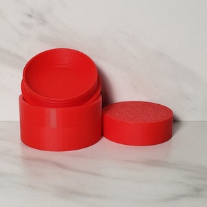 May include: A set of three red plastic containers with a smooth, rounded finish. The containers are stacked on top of each other, with the top container slightly offset from the bottom two.