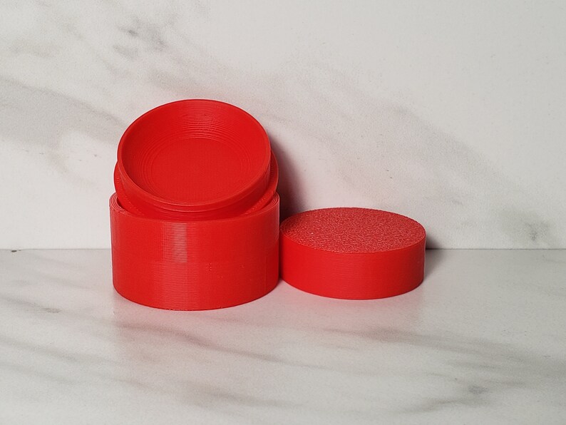 May include: A set of three red plastic containers with a smooth, rounded finish. The containers are stacked on top of each other, with the top container slightly offset from the bottom two.