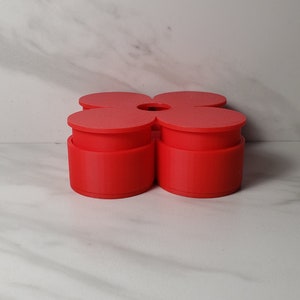 May include: A red four-sectioned flower-shaped container with a circular opening in the center.