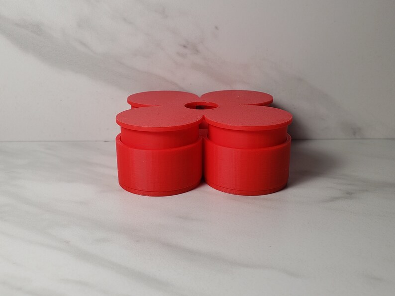 May include: A red four-sectioned flower-shaped container with a circular opening in the center.