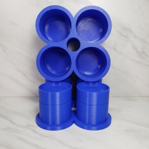 May include: A blue 3D-printed organizer with a unique design. The top section features four circular compartments arranged in a cloverleaf pattern, with a central hole. Two cylindrical containers sit below, each on a circular base. The organizer is made of solid blue plastic.