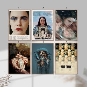 May include: Six framed movie posters for "Poor Things" are displayed. Each poster features different artwork, including portraits and artistic compositions. The posters are in various color schemes, with text that includes the movie title and credits.