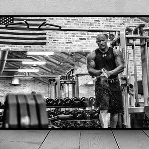 Può includere: Foto in bianco e nero di un uomo in palestra, che si allena con i pesi. Indossa una canotta nera e pantaloncini neri. La palestra è ben attrezzata con macchine per pesi e pesi liberi.