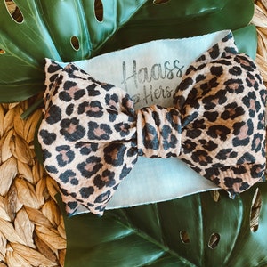 May include: A brown and black leopard print bow with the text "Haass & Hers" on a light blue background.