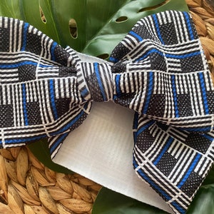 May include: A large black, white, and blue bow with a thin blue line pattern. The bow is made of a textured fabric and is tied with a white ribbon.