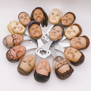 May include: A collection of 12 bottle openers, each featuring a different person's face. The bottle openers are made of metal and have a black finish. The faces are all different and unique, and they are all smiling. The bottle openers are arranged in a circle, and they are all facing the camera.