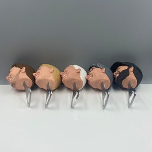 May include: Five bottle openers with different male faces sculpted on the top. Each opener is made of metal and has a silver finish.