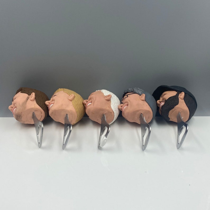 May include: Five bottle openers with different male faces sculpted on the top. Each opener is made of metal and has a silver finish.
