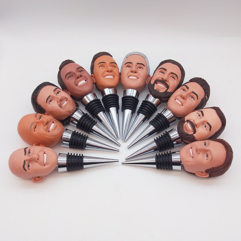 May include: A set of 10 bottle stoppers featuring different faces. Each stopper is made of a silver metal with a black base. The faces are all different and have a realistic look.