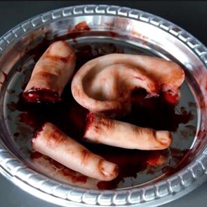 May include: A silver platter contains severed body parts, including fingers and an ear, with a pool of red liquid. The items are flesh-toned with visible details, creating a gruesome scene. The platter has a decorative edge.