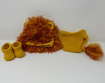 Op de afbeelding: Een gehaakt leeuwenkostuum voor een baby, bestaande uit een muts met een pluche manen, een luierhoes en slofjes. Het kostuum is gemaakt in tinten oranje en geel.