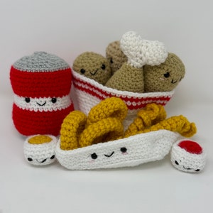 May include: A set of crocheted food toys, including a can of soda, a basket of french fries, two chicken drumsticks, and two dipping sauces. The toys are all white with red and yellow accents and have cute faces.