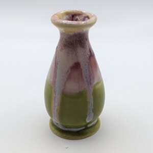 Pu&ograve; includere: Un piccolo vaso in ceramica verde con smalto rosa e bianco. Il vaso ha un corpo arrotondato e un collo stretto.