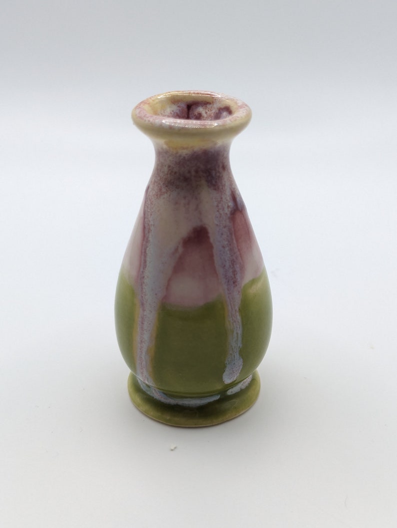 Pu&ograve; includere: Un piccolo vaso in ceramica verde con smalto rosa e bianco. Il vaso ha un corpo arrotondato e un collo stretto.