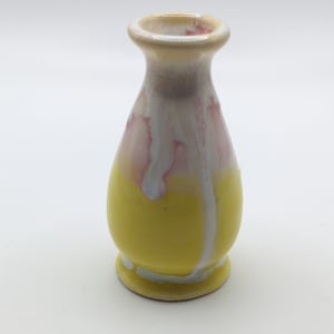 Pu&ograve; includere: Un piccolo vaso in ceramica giallo con smalto bianco e rosa. Il vaso ha un corpo arrotondato e un collo stretto.