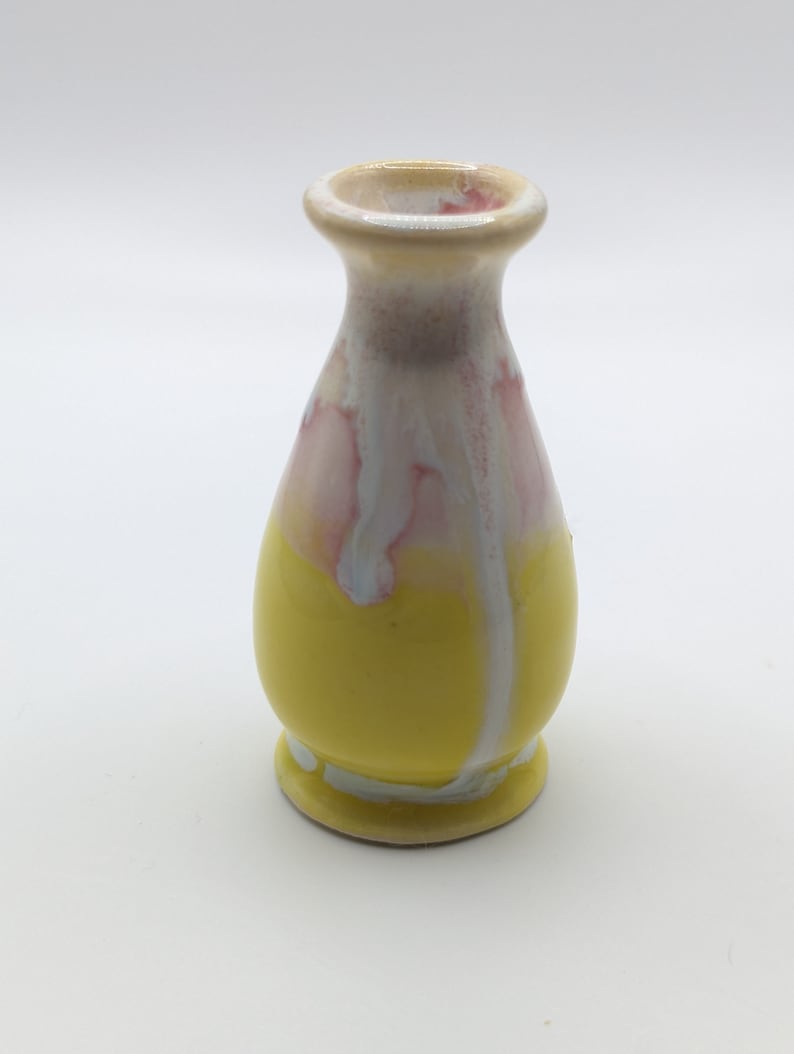 Pu&ograve; includere: Un piccolo vaso in ceramica giallo con smalto bianco e rosa. Il vaso ha un corpo arrotondato e un collo stretto.