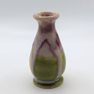 Pu&ograve; includere: Un piccolo vaso in ceramica verde e bianco con una glassa rosa e bianca. Il vaso ha un corpo arrotondato e un labbro svasato.