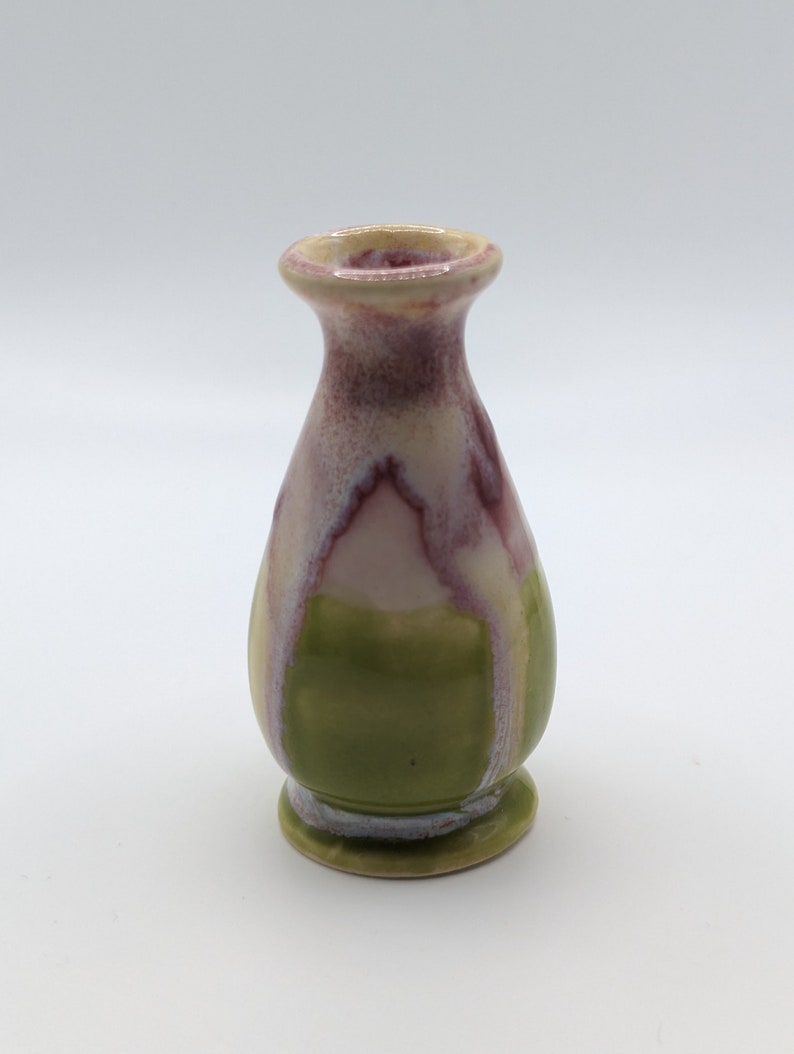 Pu&ograve; includere: Un piccolo vaso in ceramica verde e bianco con una glassa rosa e bianca. Il vaso ha un corpo arrotondato e un labbro svasato.