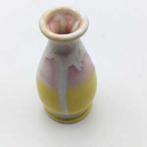 Pu&ograve; includere: Un piccolo vaso in ceramica giallo e rosa con una glassa bianca. Il vaso ha un corpo arrotondato e un collo stretto.