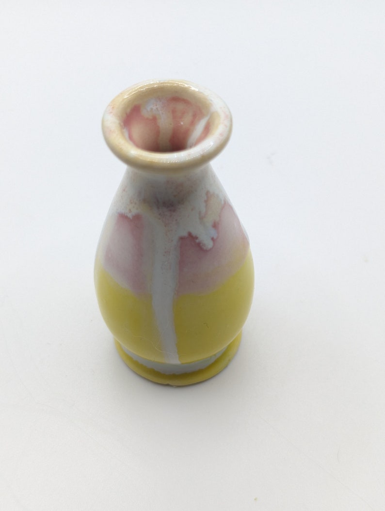 Pu&ograve; includere: Un piccolo vaso in ceramica giallo e rosa con una glassa bianca. Il vaso ha un corpo arrotondato e un collo stretto.