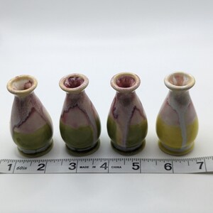 Pu&ograve; includere: Quattro piccoli vasi in ceramica con una smaltatura gialla, verde e rosa. I vasi sono allineati in una fila su una superficie bianca con un metro a nastro.