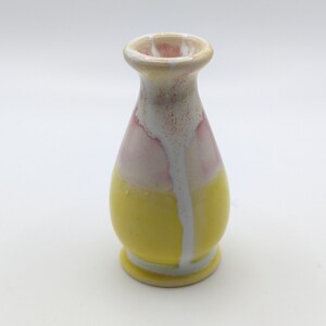 Pu&ograve; includere: Un piccolo vaso in ceramica giallo con smalto rosa e bianco. Il vaso ha un corpo arrotondato e un collo stretto.