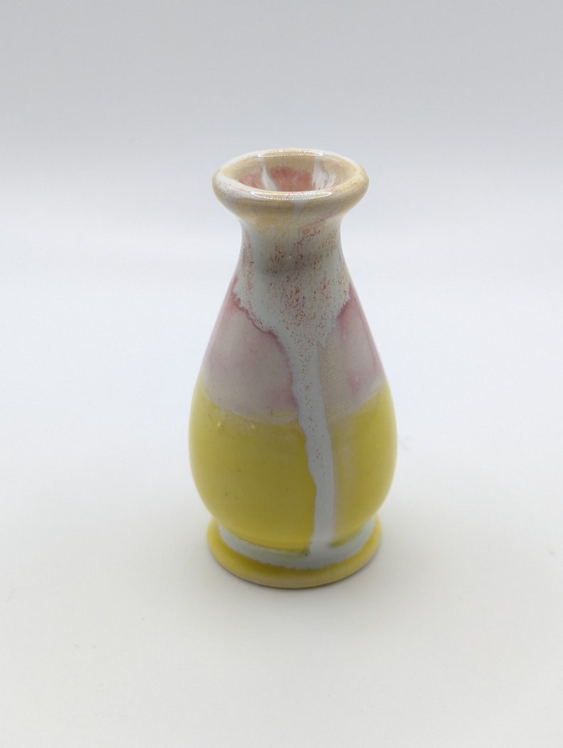 Pu&ograve; includere: Un piccolo vaso in ceramica giallo con smalto rosa e bianco. Il vaso ha un corpo arrotondato e un collo stretto.