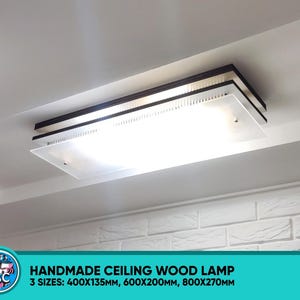 May include: A modern ceiling light fitting with a white frosted glass shade and a dark wood frame. The light is mounted on a white ceiling and is surrounded by white brick.