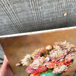 May include: A painting of a bouquet of pink, white, and peach peonies in a teal vase. The flowers are arranged in a loose, natural style and are set against a warm, brown background.