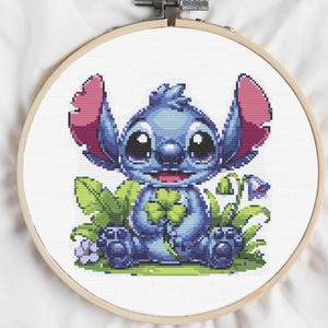 Puede incluir: Un personaje azul de Stitch de la película de Disney Lilo & Stitch sosteniendo un trébol de cuatro hojas. Stitch está sentado en un parche de trébol verde con flores rosas.