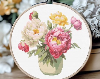 May include: A cross-stitch embroidery hoop featuring a floral design. The artwork showcases a bouquet of peonies in shades of pink, yellow, and white, arranged in a green vase. The embroidery is set against a white background, framed by a wooden hoop.