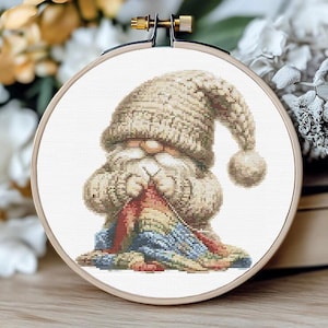 May include: A white gnome with a white knit hat and a long white beard is holding a colorful knitted blanket. The gnome is sitting on a white background.