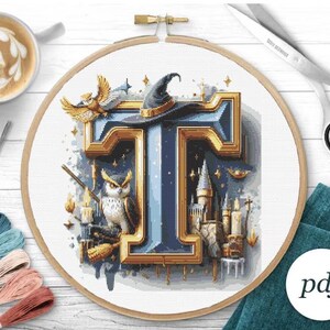 May include: A cross-stitch pattern featuring the letter "T" in a gold frame with a blue background. The letter is surrounded by magical elements, including an owl, a wizard's hat, and a castle. The pattern is available as a PDF download.