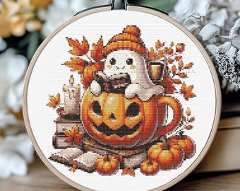May include: A cross-stitch embroidery hoop featuring a Halloween-themed design. The image shows a smiling ghost wearing an orange hat, sitting in a carved pumpkin mug. The design includes pumpkins, autumn leaves, books, and a candle. The hoop is approximately 6 inches in diameter.