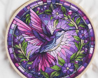 May include: A cross-stitch embroidery of a hummingbird in a stained-glass style. The design features a hummingbird with purple, pink, and blue hues, surrounded by flowers and leaves. The embroidery is set in a wooden hoop.