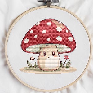 May include: A cross-stitch embroidery of a red and white mushroom with a white stem and a cute face. The mushroom is surrounded by green leaves and red flowers.