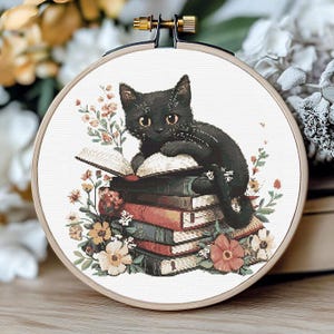 Peut inclure: Un chat noir assis sur une pile de livres avec des fleurs autour de la base. Le chat regarde vers la gauche et a un livre dans ses pattes.
