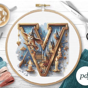 May include: A cross-stitch pattern featuring the letter V, a castle, owls, and candles. The letter V is gold with a blue background. The castle is a light blue color with gold accents. The owls are brown and white with blue hats. The candles are white with gold accents. The pattern is in a round hoop.