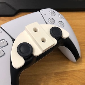 Puede incluir: Un accesorio de plástico blanco con dos botones negros para un mando blanco de PlayStation 5.