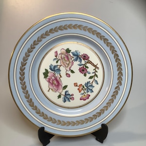 May include: A blue and white porcelain plate with a gold rim and a floral design. The plate has a delicate floral pattern in pink, blue, and yellow.