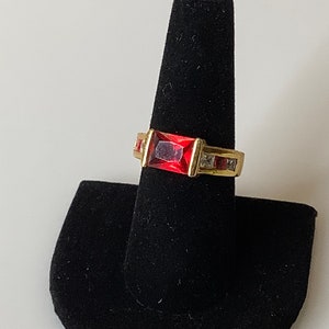 May include: A gold ring with a large, rectangular, red gemstone surrounded by smaller, clear gemstones.