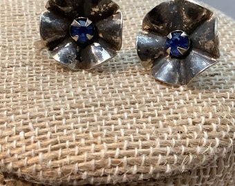 May include: A pair of silver flower-shaped earrings with blue gemstone accents.