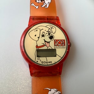 May include: Red and orange plastic watch with a digital display and a cartoon Dalmatian dog on the face. The watch band has a repeating pattern of Dalmatian dogs and bones. The watch face says "101 Dalmatians" and "©Disney".