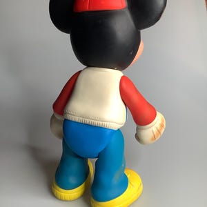 May include: A vintage Mickey Mouse figure, viewed from the back, wearing a red cap, a white vest, red sleeves, blue trousers, and yellow shoes. The figure has large black ears and a black head. The figure is approximately 46 cm tall.