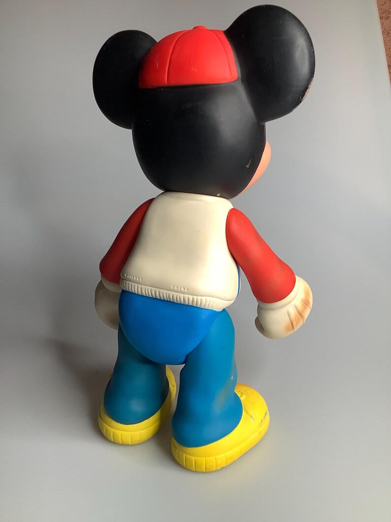 May include: A vintage Mickey Mouse figure, viewed from the back, wearing a red cap, a white vest, red sleeves, blue trousers, and yellow shoes. The figure has large black ears and a black head. The figure is approximately 46 cm tall.