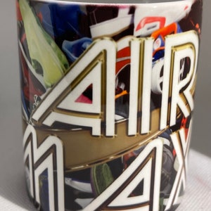 May include: White ceramic mug with a colorful collage of sneakers and the words "AIR MAX" in gold and white lettering.