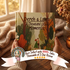 May include: A personalized book cover with the title "Derek & Laura: A Thousand Little Moments." The cover features an illustration of a couple in a forest setting with autumn colors. The book is held by a person.