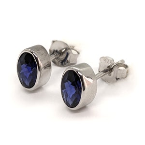 May include: A pair of silver stud earrings with a dark blue gemstone in each. The earrings are marked with "925" on the back.